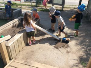 Children work together, using a pipe as a chute from the planter box.