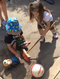 A boy and girl use a broom, toy truck and volleyball to mimic cleaning up a construction site.