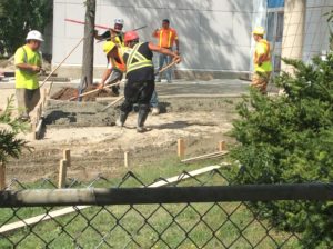Construction workers spreading concrete with shovels and rakes at a building site.