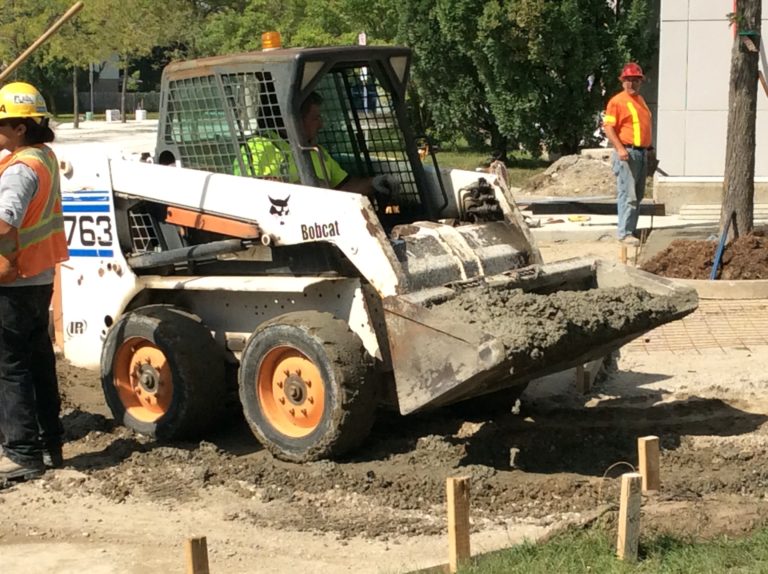 Bobcat machine spreading cement at a construction site.