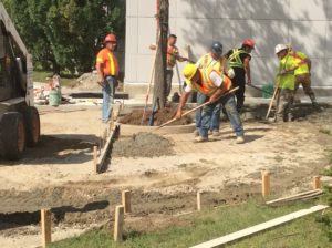 Group of construction workers leveling cement with rakes outside a building.