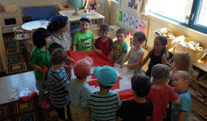 Children with teacher in a classroom gathered around table with a large Canadian flag on it.
