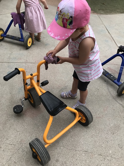 child wearing pink is playing with orange trike