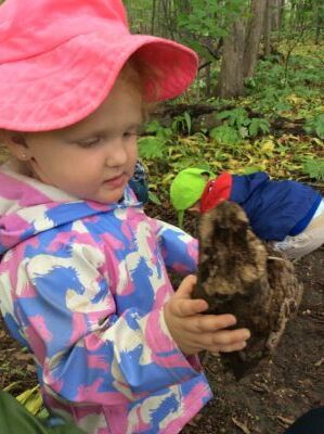 Girl in a pink hat carefully holding a large piece of tree bark.