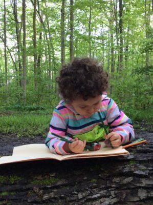 Girl lying on a log and drawing in a sketchbook with pencil crayons.