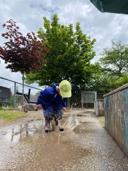 child jumping in a puddle with rainboots