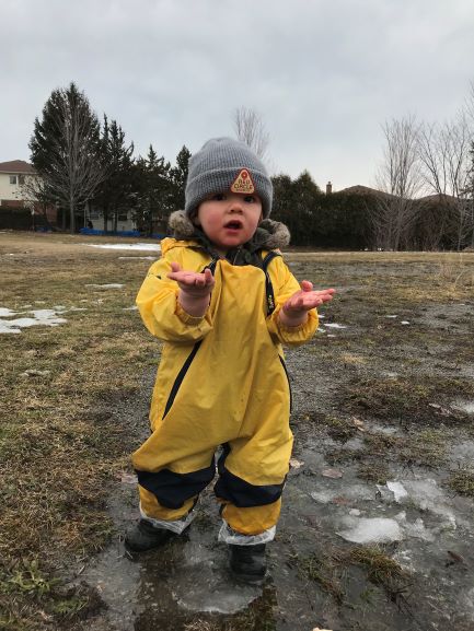 Toddler in a yellow rain suit standing in muddy field.