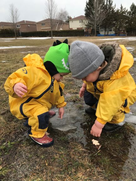 Two young children crouched together near a small puddle.