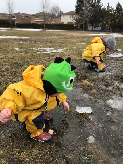 Two children in yellow rain suits squatting near icy puddles.