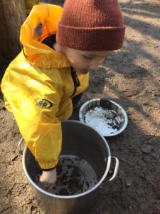 Child exploring textures while mixing mud in a large outdoor pot.