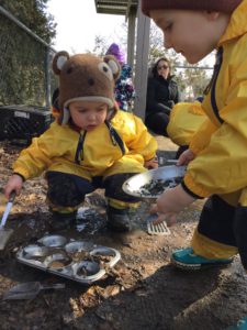 Children making pretend mud pies using trays and scoops outside.