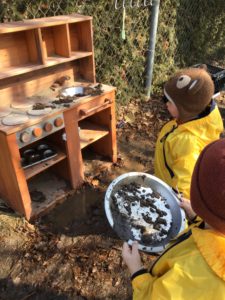 Children putting pretend mud pies into an outdoor play kitchen stove.