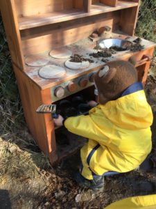 Child placing pots inside the pretend oven of outdoor mud kitchen.