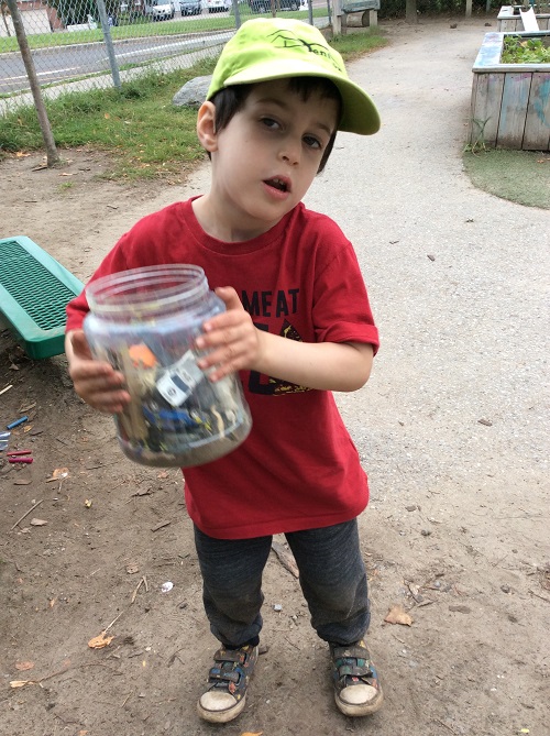 Little boy holding a plastic jar filled with small toys, using it as a homemade shaker instrument.