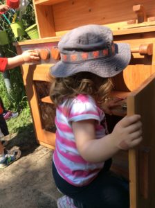 Child crouched down in front of the play kitchen, opening a lower cabinet door.