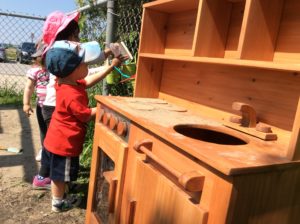 Two children standing and playing in front of play kitchen.