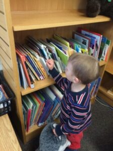 Child selecting a book from a low library shelf.