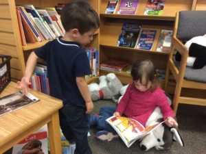 Two children sitting on the floor reading books together.