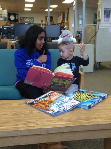 Teacher reading to a toddler sitting on a couch.
