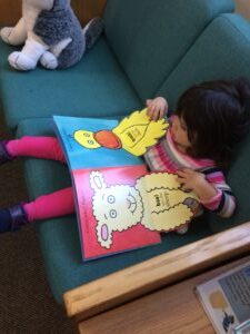 Toddler lying on a couch looking through a colourful picture book.