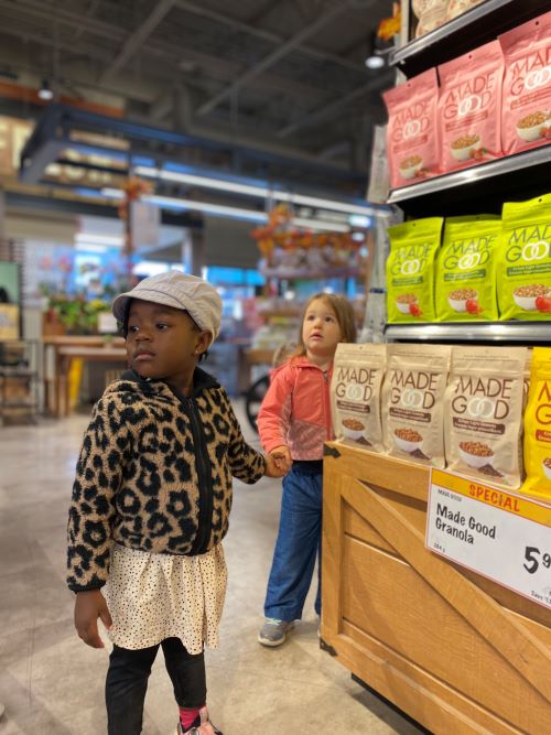 Two small girls in snack aisle of grocery store.