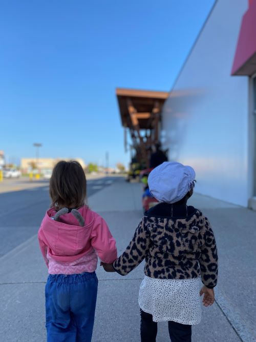 two children holding hands walking on sidewalk