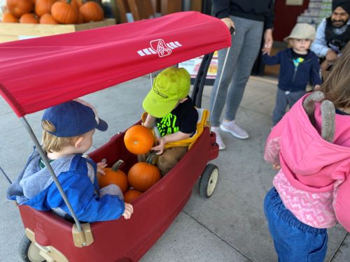 Two children in wagon with pumpkins.