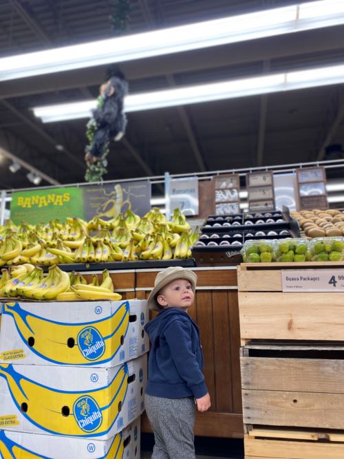 Child in grocery stores beside banana display shelf.