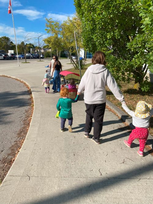 Children and educator walking hand in hand along sidewalk.