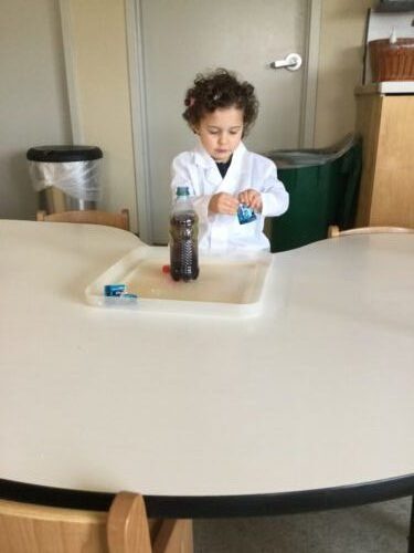 Child dressed in lab coat at table, preparing a science experiment.