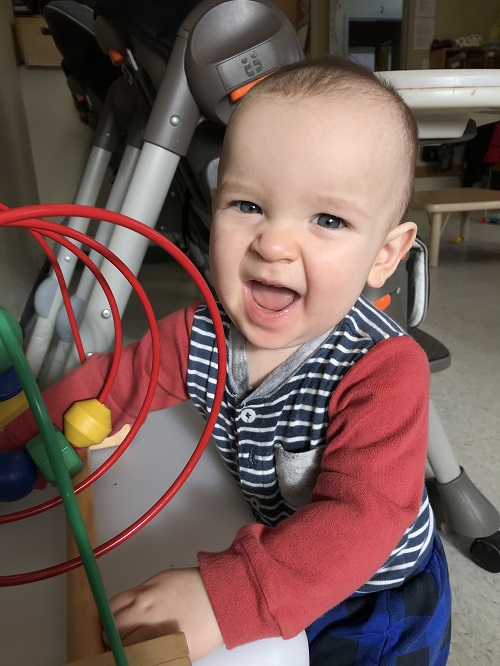 Infant smiling while playing with a bead maze toy in a child care setting.