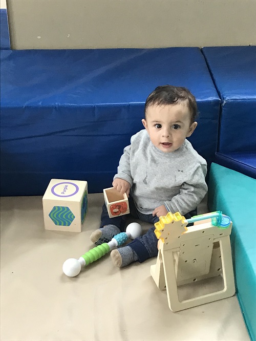 Young child sitting on soft mat exploring blocks and toys in an early learning environment.