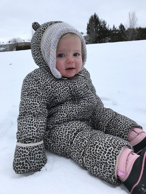 Infant dressed in a leopard print snowsuit sitting in the snow during outdoor play.