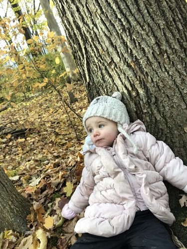 Little girl sitting at the bottom of tree, leaning against it in an autumn forest