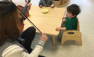 Child sitting at a table watching Seneca College student play violin.