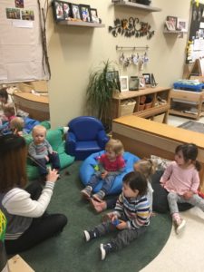 Group of young children sit in a circle with Seneca College student, watching violin demonstration.