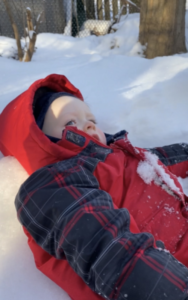 Child wearing red jacket and hood laying down on the snow