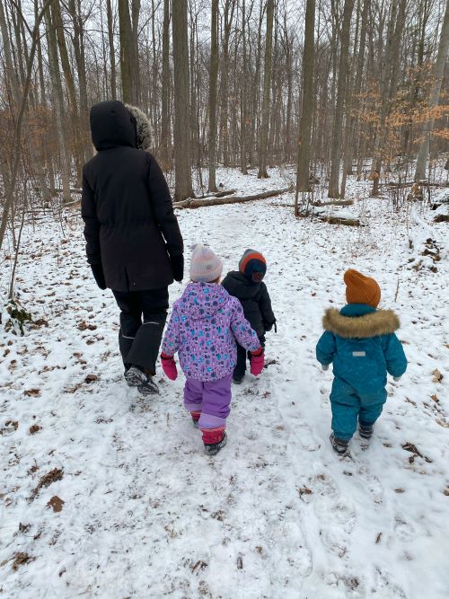 children and educator walking in a snowy forest, view from behind